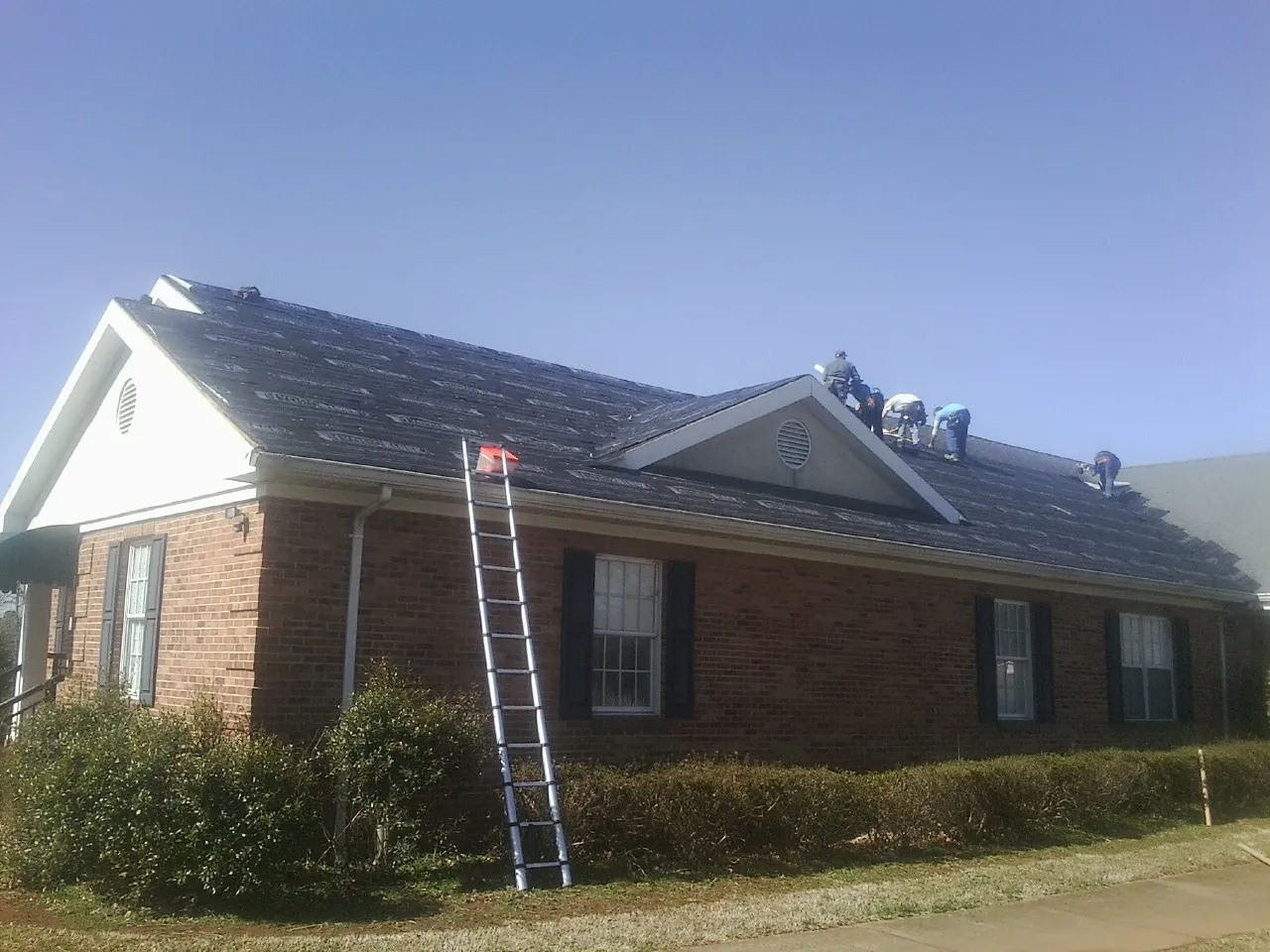 Crew tearing shingles off a brick ranch roof with a ladder set — Metal Roof Repair work by our crew in Calabasas