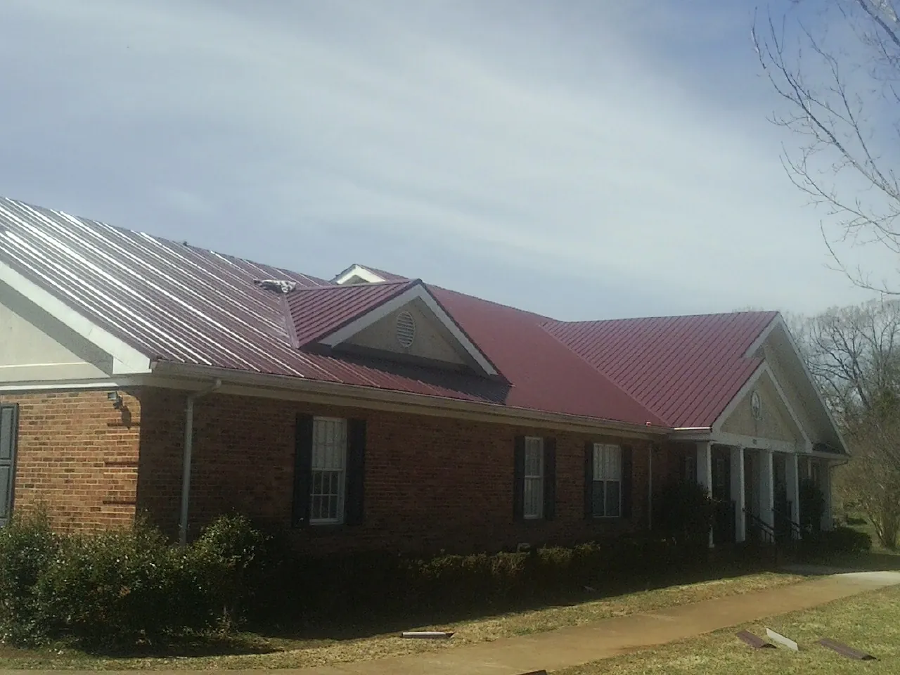 Red metal roof with gabled entries on a long brick building, from a Hail Damage Roof Repair job in Calabasas