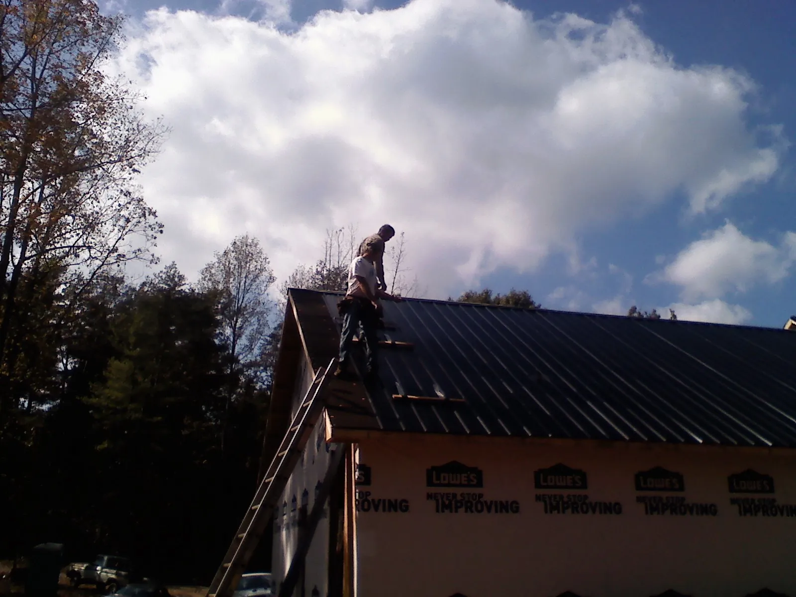 Roofer fastening dark metal panels high against a cloudy sky, from a Roof Inspection job in Calabasas